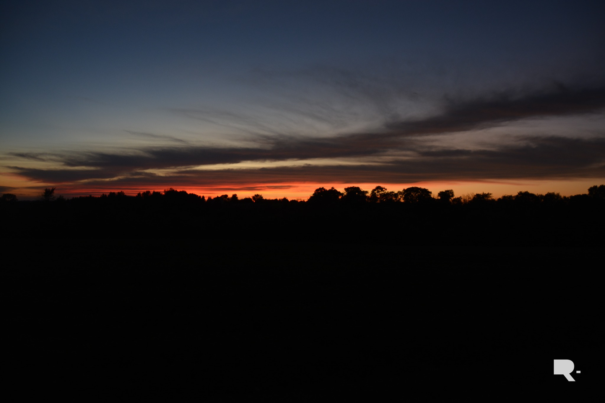 Dark rural landscape beneath a vivid red and orange sunset